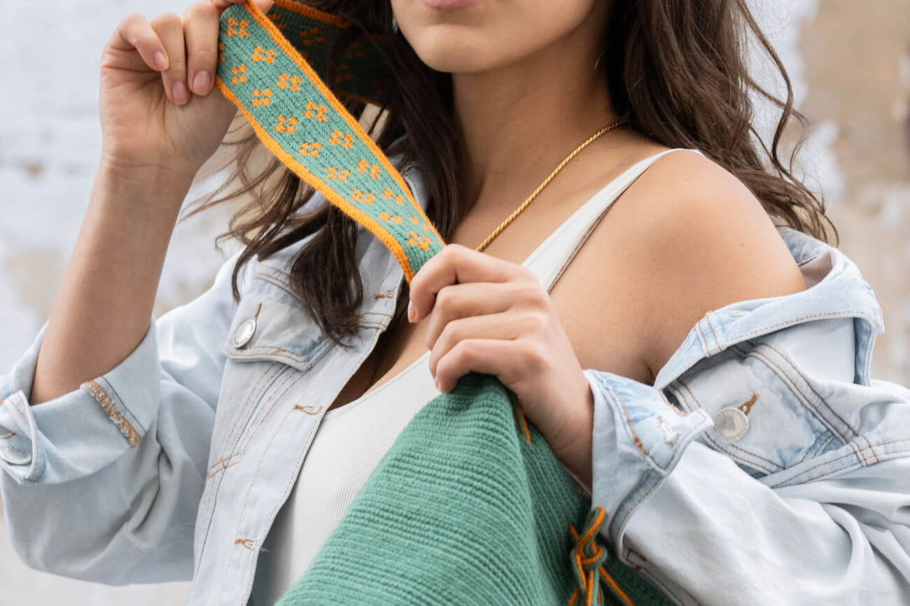 Model wearing a jean jacket and white shirt putting on a teal colored bag.