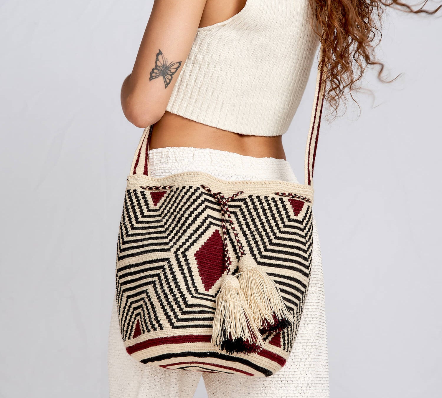 Model in white clothing wears a beige, black and maroon bag