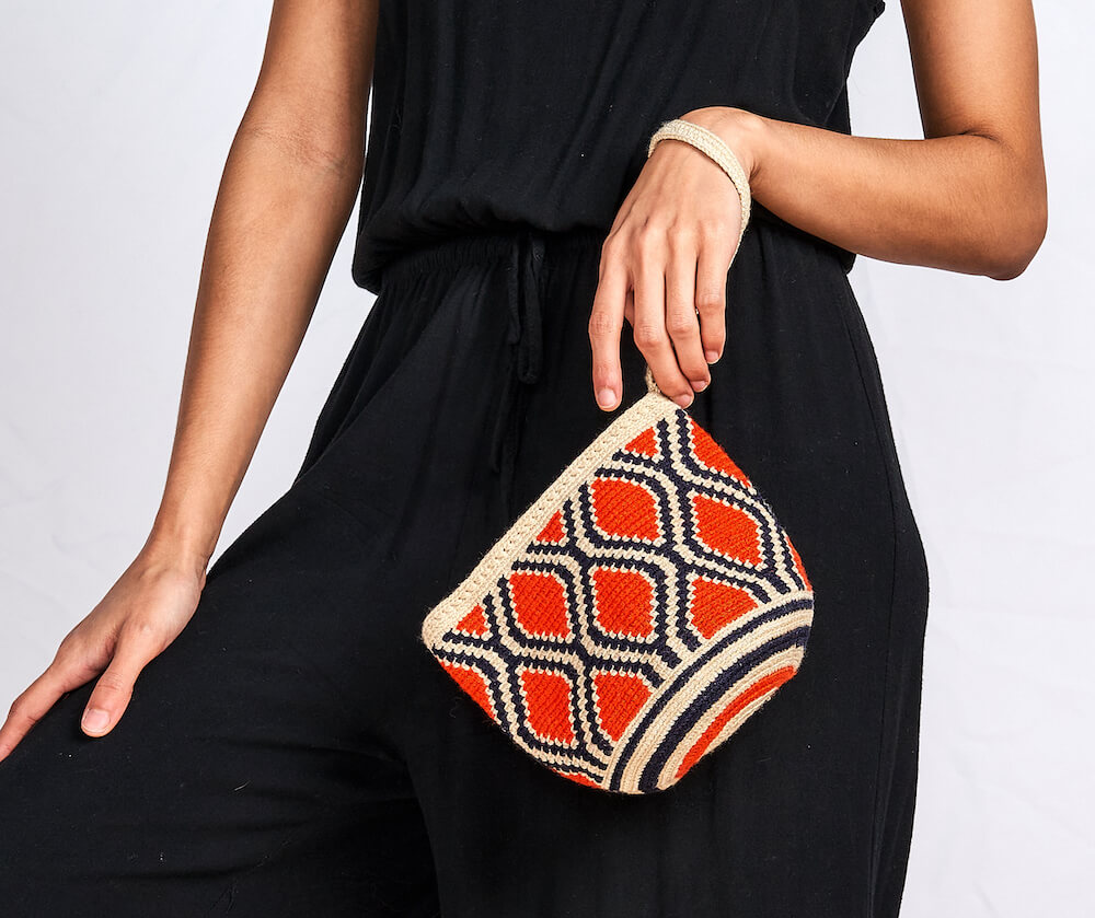 Model in a black jumpsuit holds a clutch/wristlet.