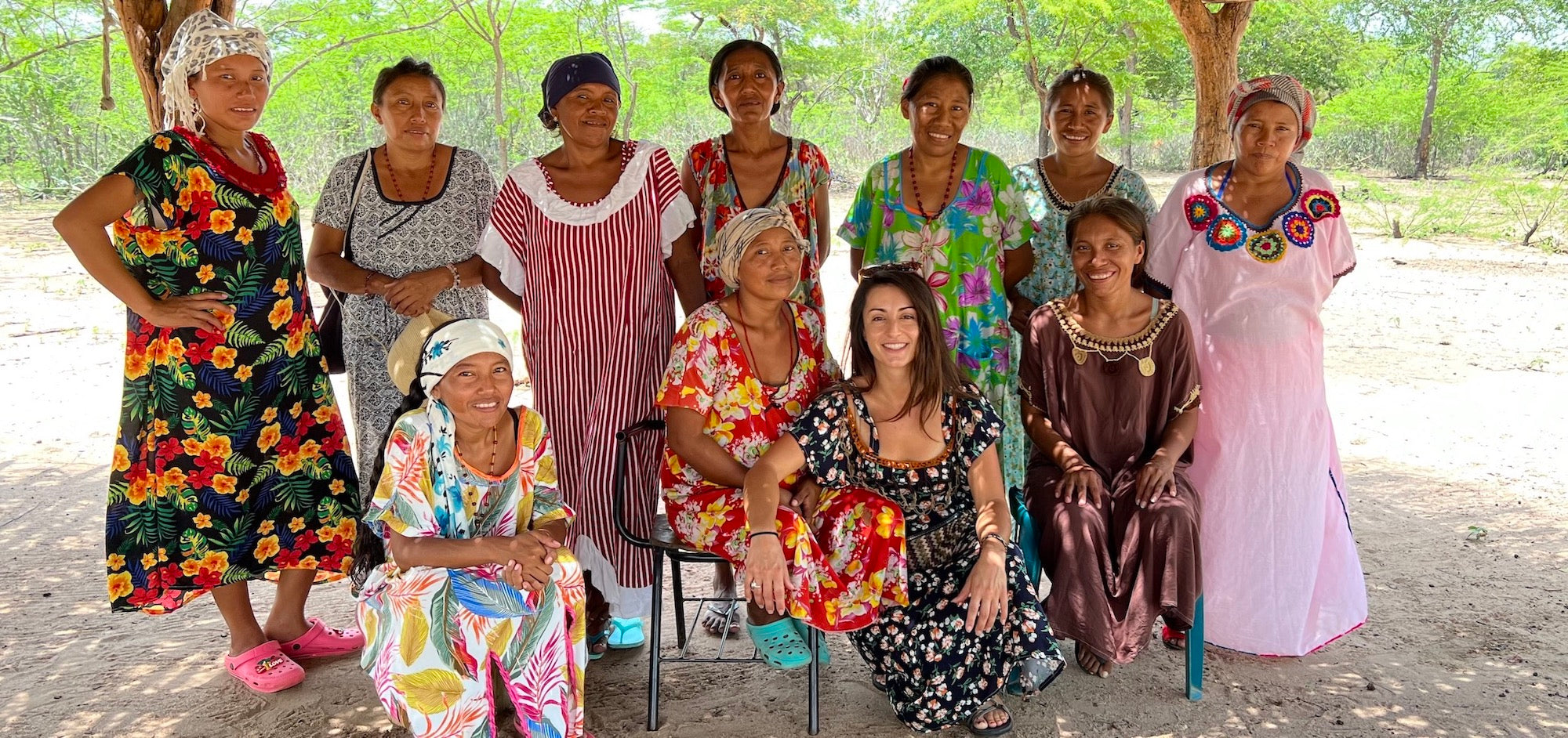 Group of Wayuu women in colourful dresses under a traditional "enramada" 